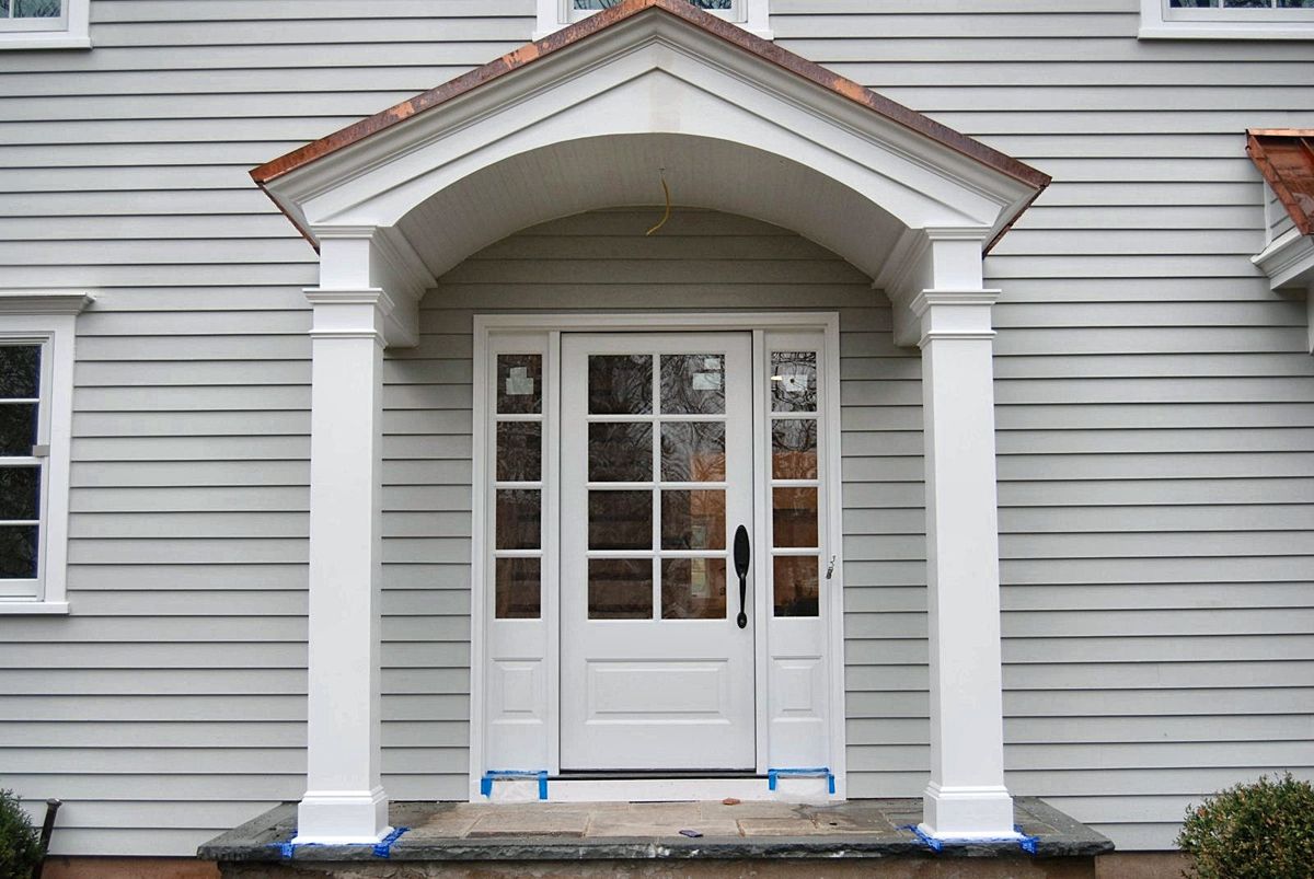 Arched portico with square columns and a copper roof over a paneled front door